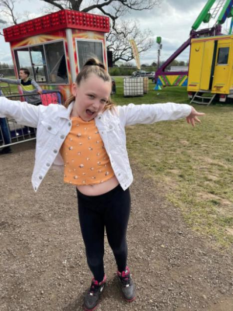 A young girl, Brooke Wiggins, with her arms out in front of carnival rides.