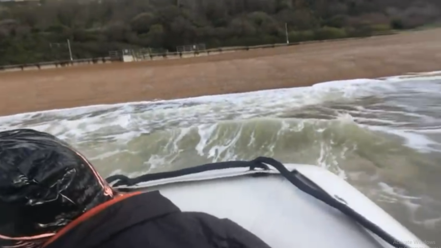 View from a boat as it enters the choppy sea from a sandy beach, with a shoreline and trees in the background.