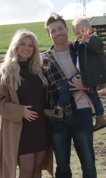 A pregnant woman, a man, and a young child smiling together.