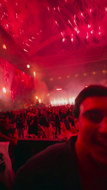 A person in the foreground taking a selfie with a crowd and stage pyrotechnics in the background.