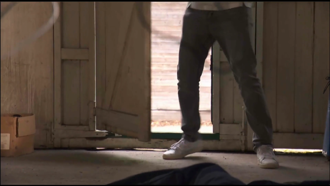 A person in grey pants and white sneakers walking through a doorway.