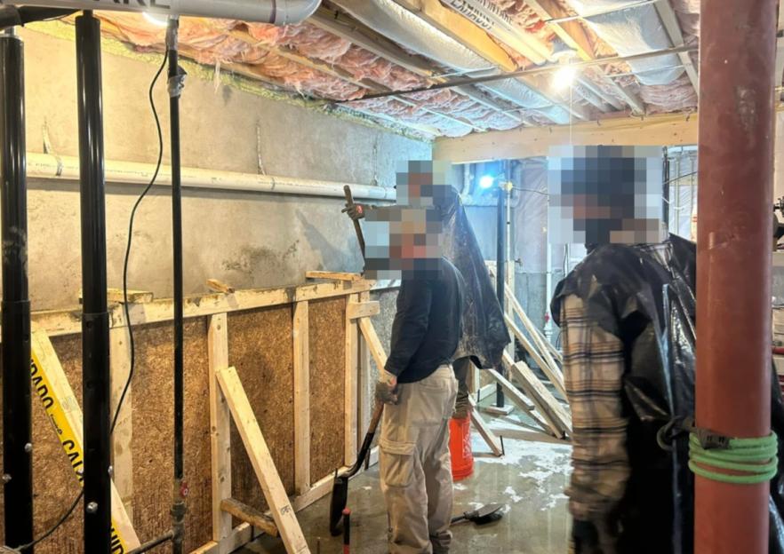 Several men working in a basement with exposed insulation and pipes, preparing to pour concrete.