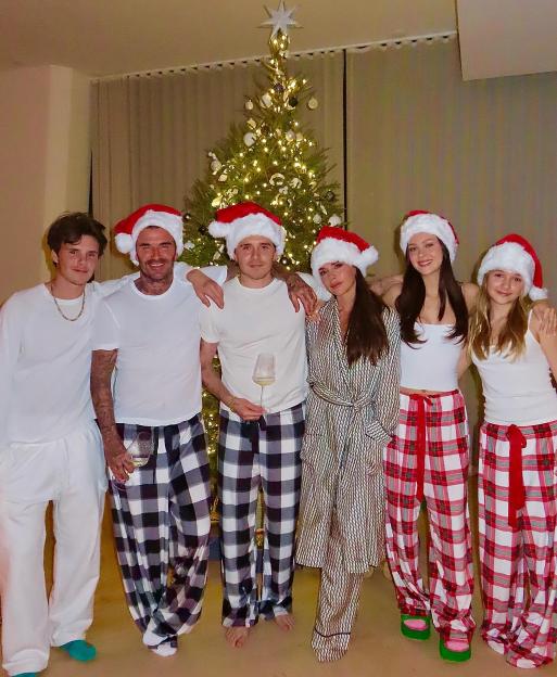 The Beckham family in matching pajamas and Santa hats in front of a Christmas tree.