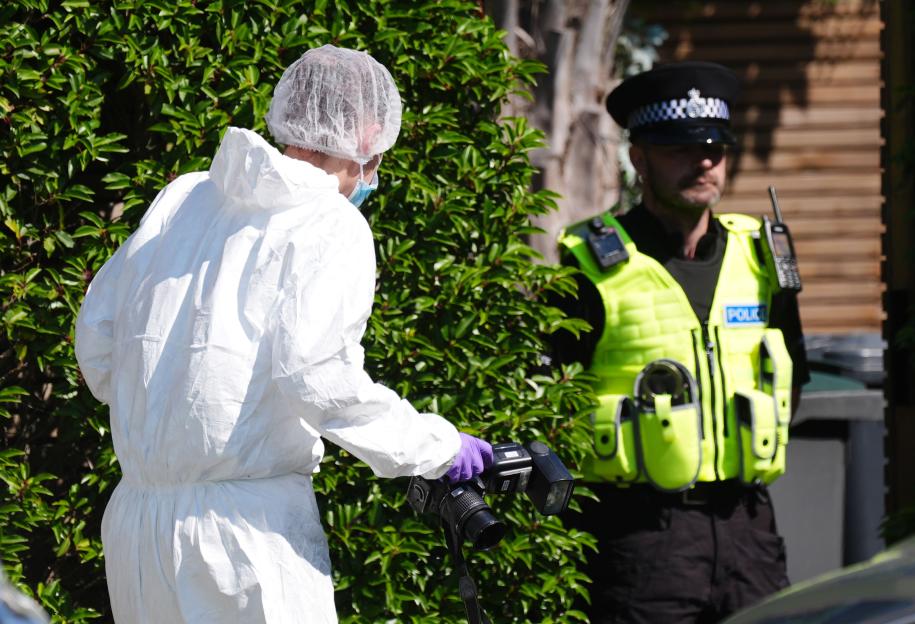 Forensic technician taking photos at a crime scene with a police officer in the background.