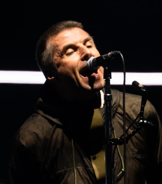 Liam Gallagher singing into a microphone on stage.