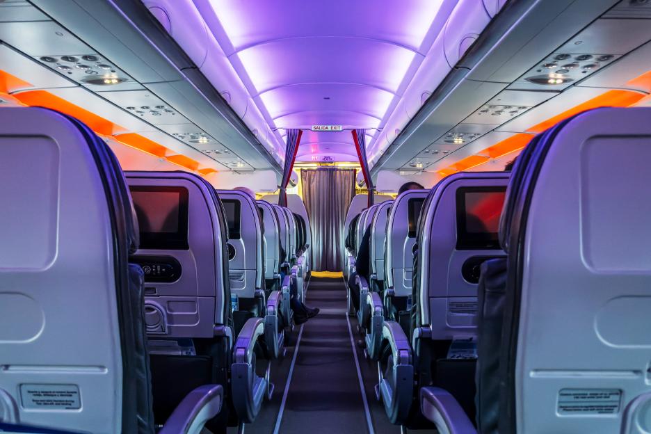 Airplane cabin aisle with purple and orange mood lighting during a night flight.