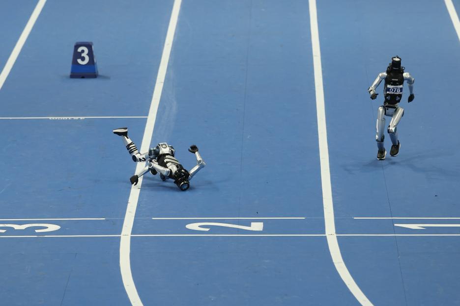 A humanoid robot has fallen on a blue track next to the lane 2 marker while another humanoid robot runs in lane 3.