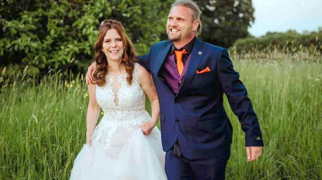 Photo of Christopher and Kayleigh Coll, a couple smiling and walking arm-in-arm through a grassy field.