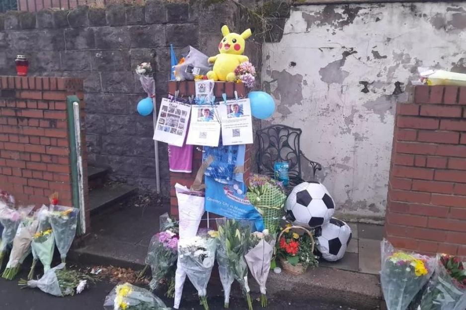 A memorial with flowers, balloons, a Pikachu plushie, and soccer balls on a street.