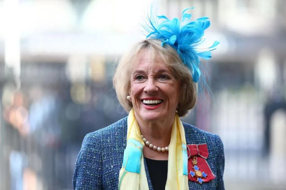 British journalist Esther Rantzen smiling, wearing a blue hat with feathers, a blue jacket, and a medal pinned to her chest.