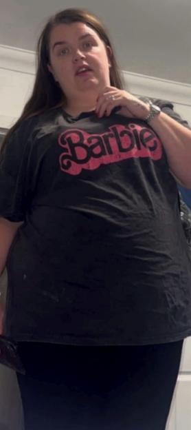 A woman with long dark hair, wearing a black Barbie t-shirt.