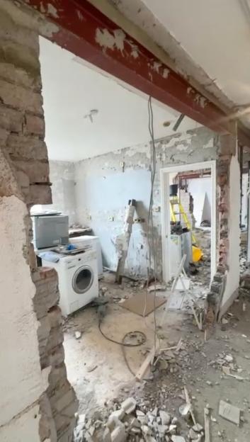 Interior of a home under demolition with exposed brick, an I-beam, and debris on the floor.