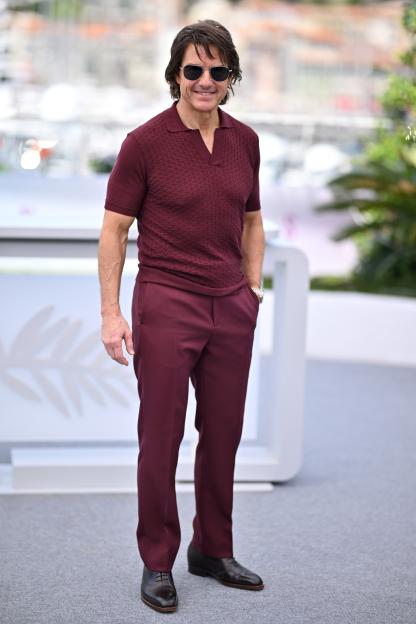 Tom Cruise in a maroon polo shirt and matching pants, wearing aviator sunglasses, at the Mission Impossible photocall.