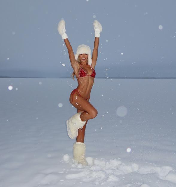 Molly Smith poses in a red bikini, white mittens, and white fur hat and boots in a snowy landscape.