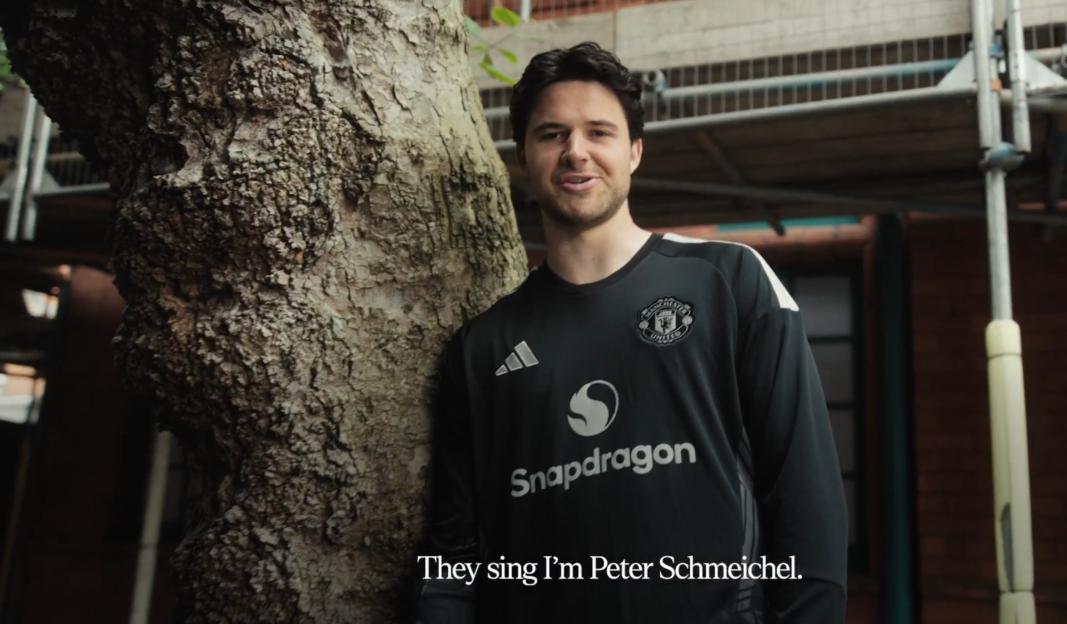 A man in a black Manchester United Snapdragon jersey with text "They sing I'm Peter Schmeichel" on the bottom of the screen.