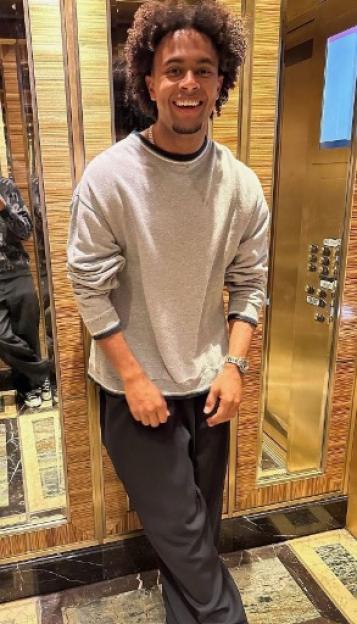 A man with curly hair smiling in an elevator with his reflection in a mirror.
