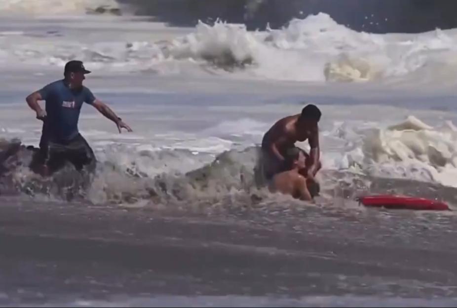 A man helps a drowning boy in rough ocean waves as another man approaches.