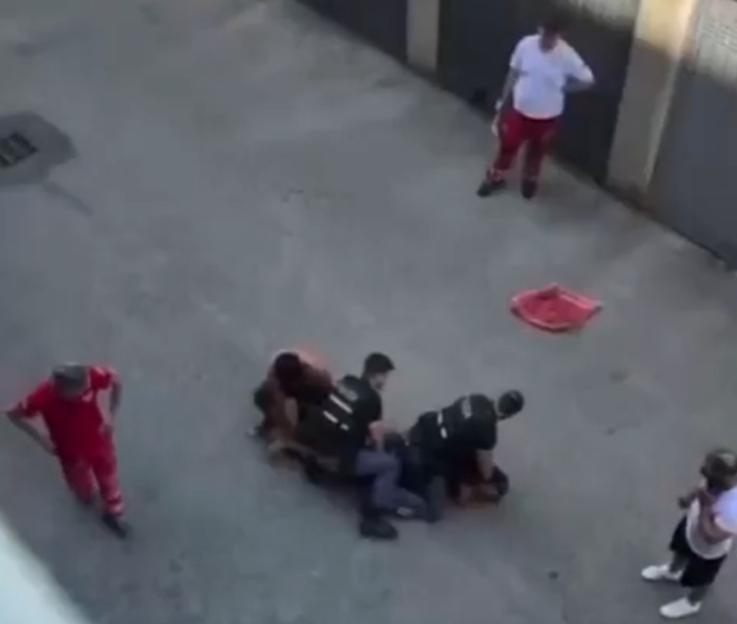 A Moroccan man is pinned to the ground by two police officers, while two other individuals in red uniforms and one in white stand nearby.