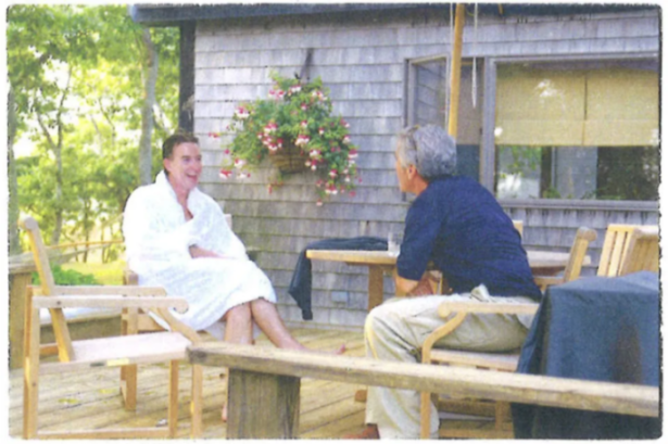 Two men seated on a wooden deck, talking to each other.