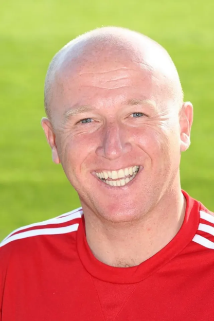 A man with a shaved head and a red shirt smiling at the camera.