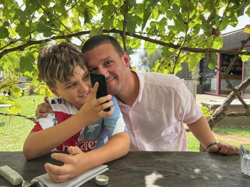A man and a boy taking a selfie under a leafy canopy.