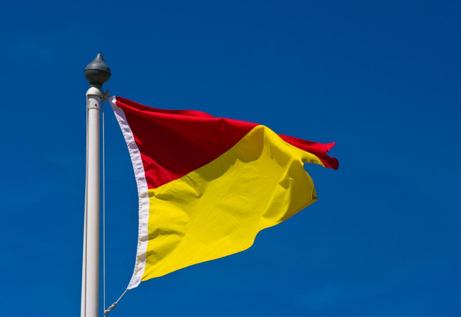 Red and yellow lifeguard flag flying against a clear blue sky.