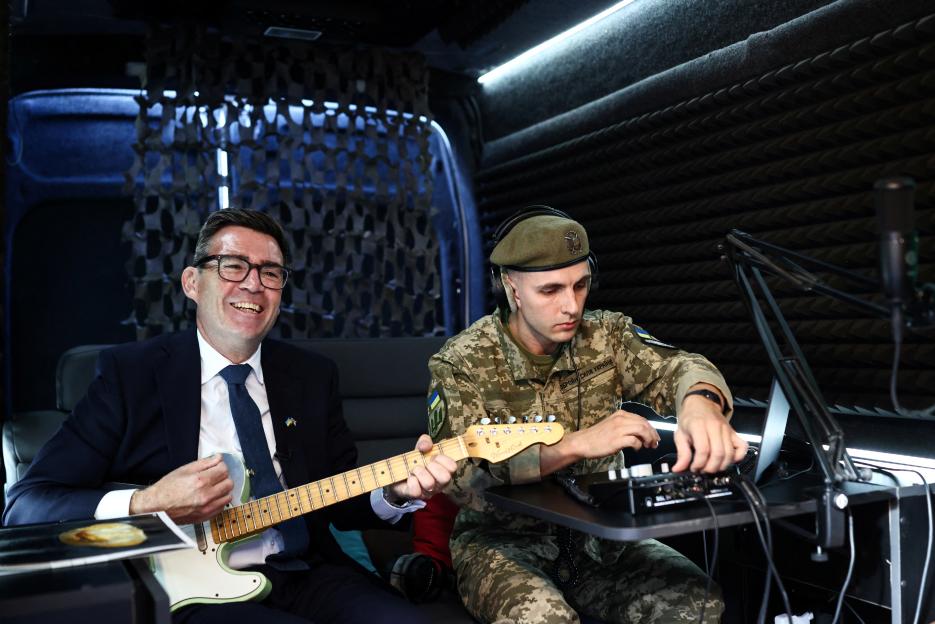 Britain's Prime Minister Andy Burnham plays the guitar next to a Ukrainian soldier in a mobile recording studio.
