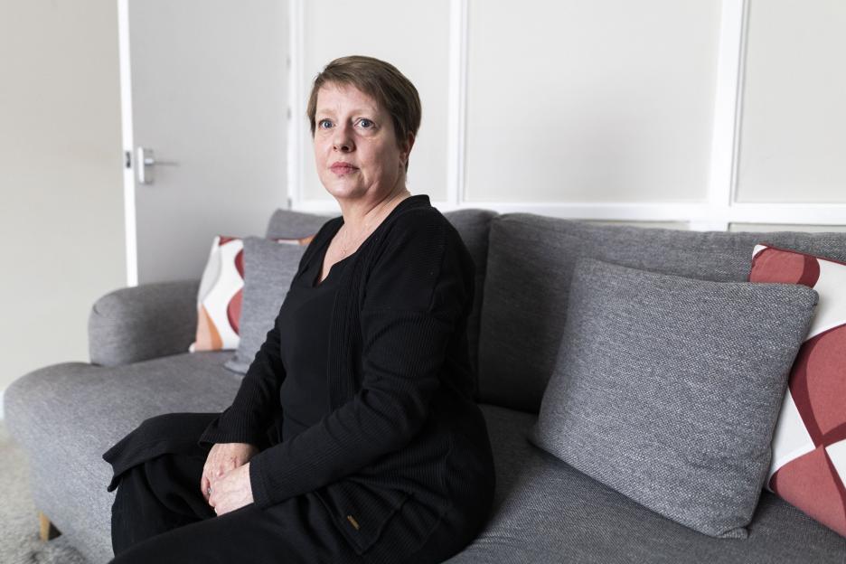 Natalee Gibbings, a woman who was raped in her bedroom, sits on a gray sofa in her home.