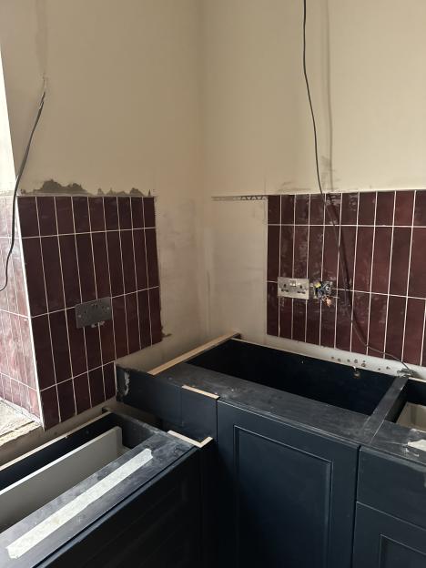 Partially tiled kitchen with dark blue unfinished cabinetry and exposed electrical wires.