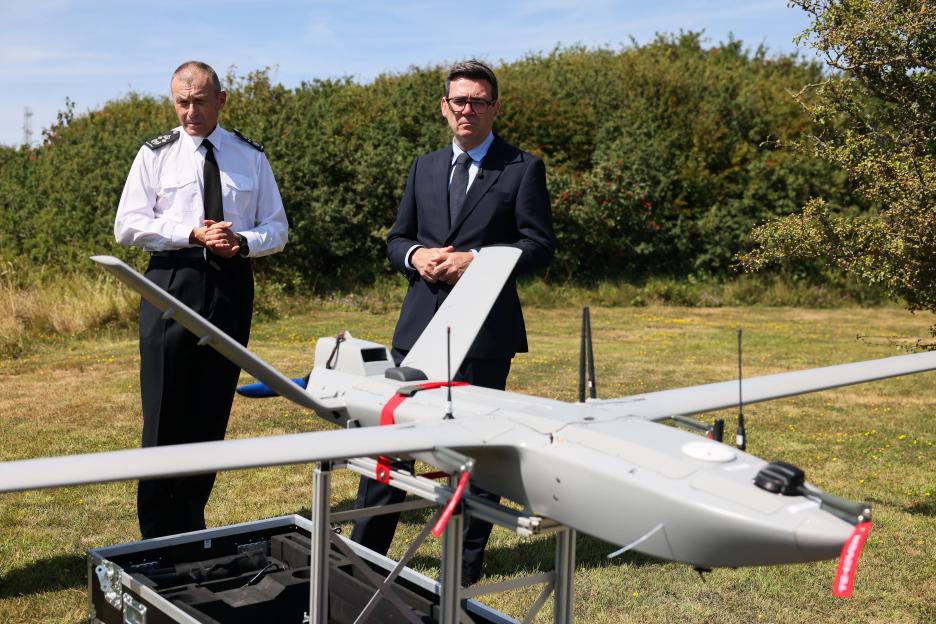 Britain's Prime Minister Andy Burnham and Duncan Capps, Border Security Commander, stand behind a surveillance drone.