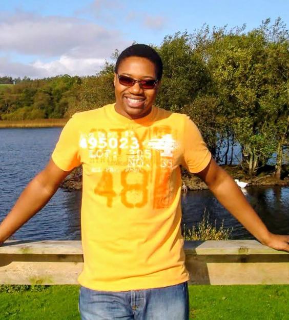 Mark Tshuma, an IT manager, smiling while standing outdoors in front of a lake.