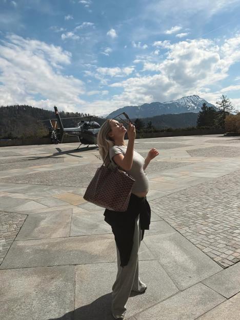 Pregnant woman posing outdoors with a helicopter and mountains in the background.