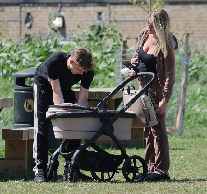 Freddy Brazier bending over baby Isla's stroller with Holly Swinburn in a park.