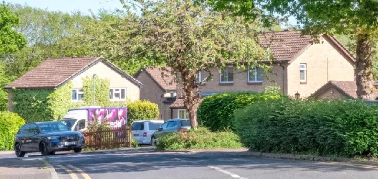 Street sign for Oaks Dene, a residential road with houses and cars.