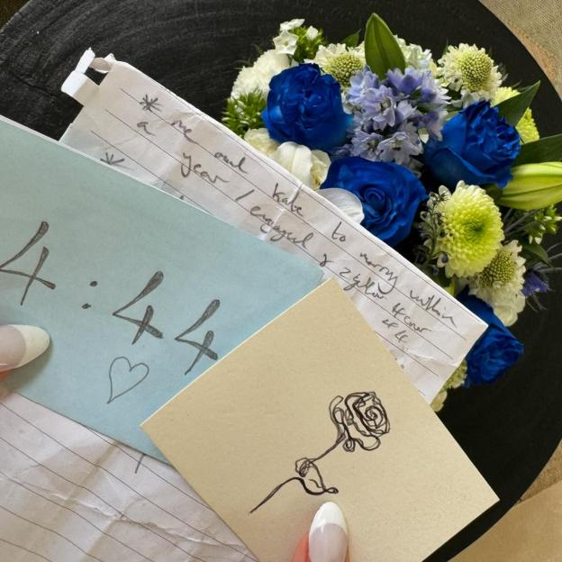 A white, light blue, and beige collage of notes with handwritten messages, a rose drawing, and a bouquet of blue and white flowers.