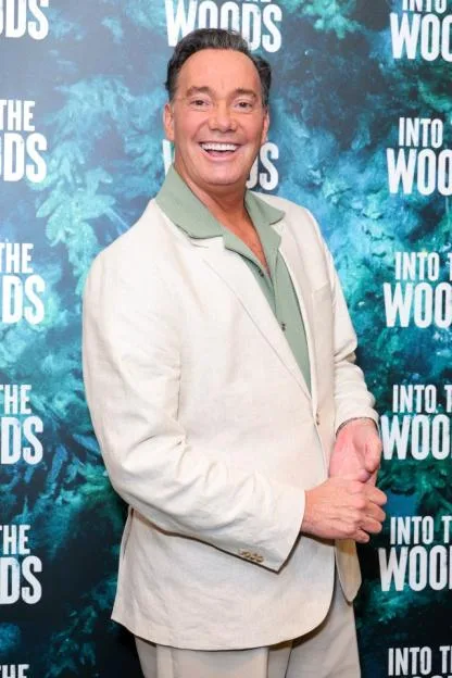 Craig Revel Horwood smiling in front of an "Into The Woods" backdrop.