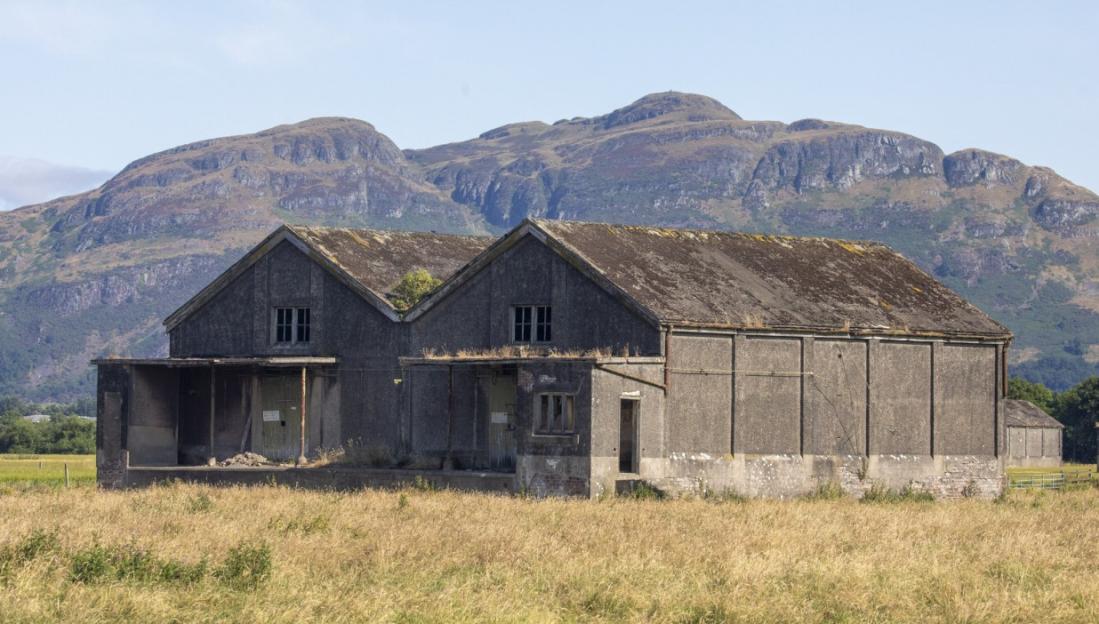 Two concrete World War 1 naval bomb depot buildings in a field with mountains in the background.