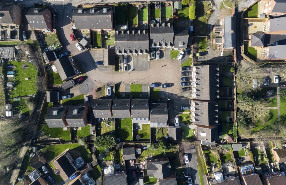 Aerial view of a residential neighborhood with houses, cars, and green spaces.