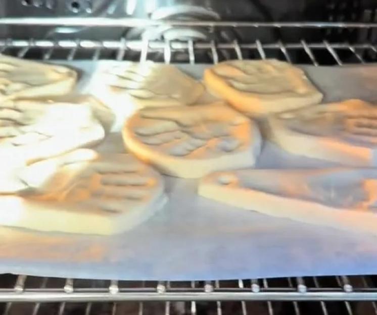 Salt dough ornaments with hand and foot prints baking in an oven.