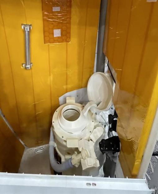 A mockup of the Universal Waste Management System, a toilet for astronauts, inside a narrow compartment with golden walls.