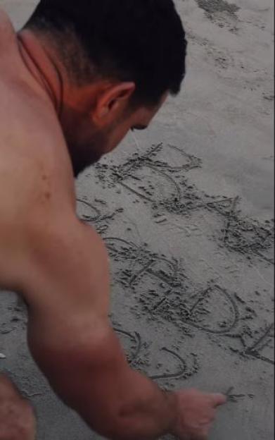 Gaz Beadle drawing "BABY" in the sand to announce his girlfriend Maia's pregnancy.