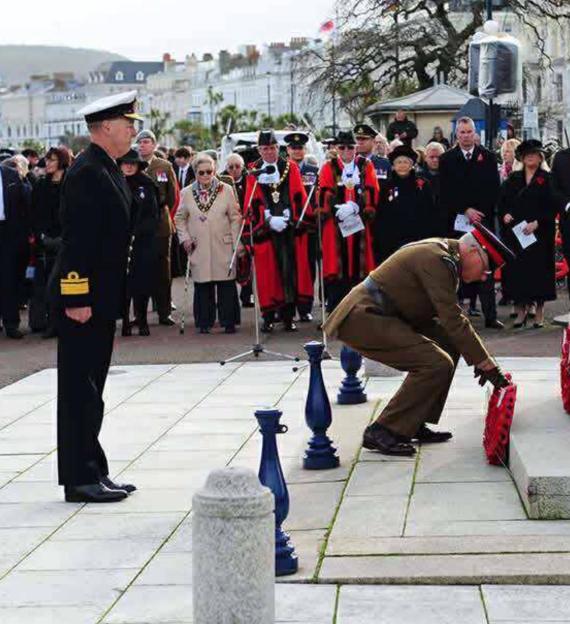 A man in a military uniform places a red wreath on a stone monument.