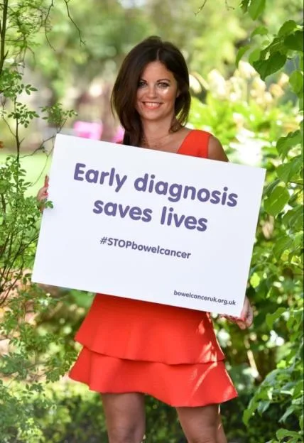 A woman in a red dress holds a sign that reads "Early diagnosis saves lives" and "#STOPbowelcancer."
