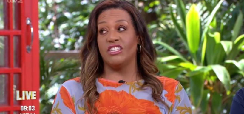 A woman with long brown hair and a floral shirt looks to her right with an open mouth.