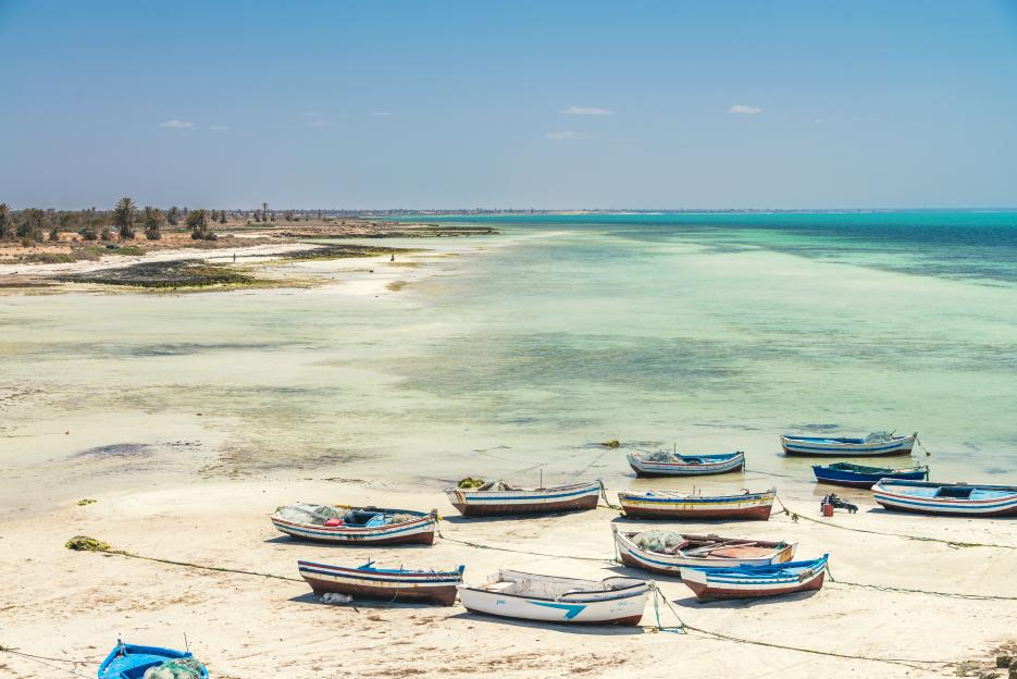 Djerba Island shoreline with boats on the sandy beach and clear turquoise waters.