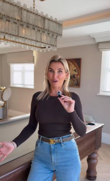 Billie Faiers holding a small microphone in a room with a large chandelier and a pool table.