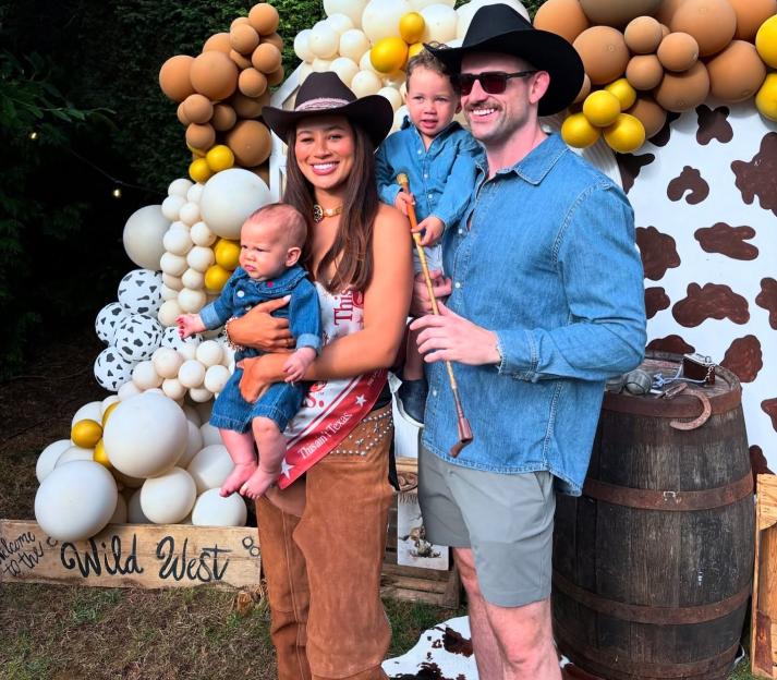 A family of four dressed in cowboy attire standing in front of a balloon arch and a "Welcome to the Wild West" sign.