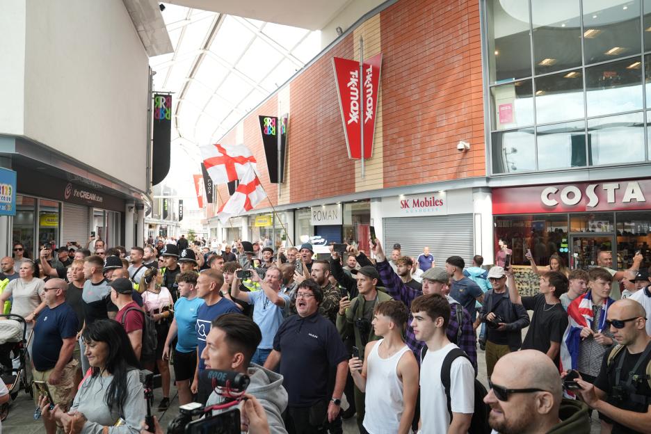 Anti-immigration protesters in a shopping centre, with some holding up English flags and others filming with phones.