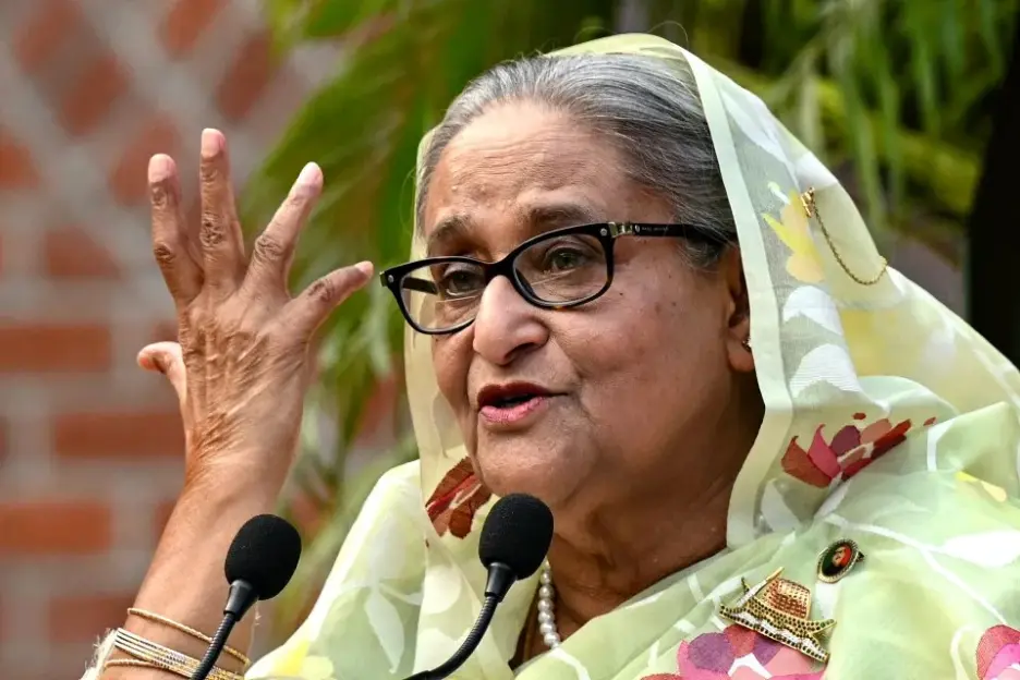 Sheikh Hasina speaking at a microphone, gesturing with her right hand.
