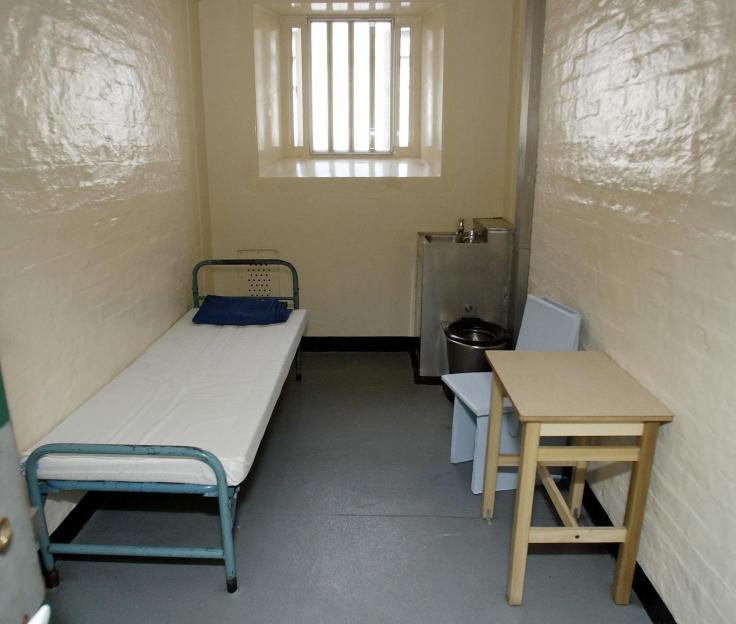 A prison cell at HMP Wakefield with a bed, toilet, and small table with two chairs.
